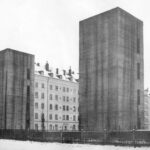 Zwei hohe dunkelgraue Häuser rechts und links, dazwischen ein helles hohes Haus mit vielen Fenstern: Bauen im Nationalsozialismus.