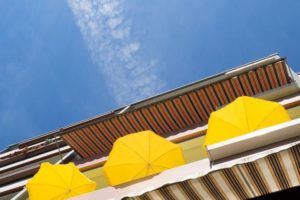 Gegen Sommerhitze: Drei gelbe Sonnenschirme auf Balkon unter blauem Himmel.