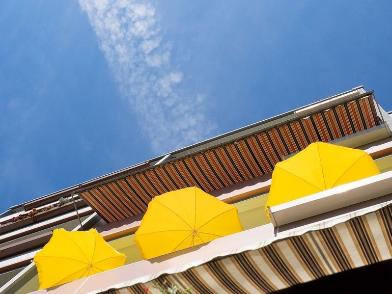 Gegen Sommerhitze: Drei gelbe Sonnenschirme auf Balkon unter blauem Himmel.